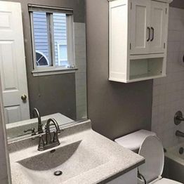 Small bathroom with sink, mirror, white cabinet, and tiled bathtub.