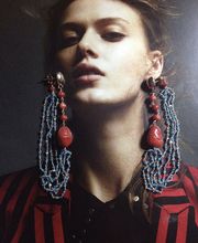 Frau trägt große Ohrringe und rot-schwarz gestreifte Kleidung, schaut nach vorne.