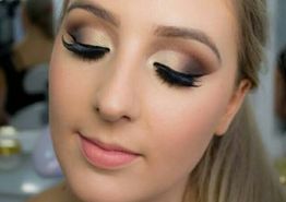 Mulher com maquiagem elaborada nos olhos, sombra marrom e dourada, cílios longos e batom rosa.