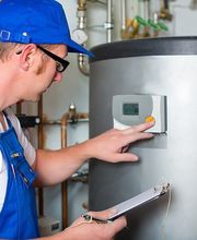 Techniker in blauer Latzhose prüft eine Heizungsanlage und notiert Messwerte auf einem Klemmbrett.