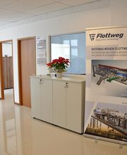 Corredor de escritório com banner da Flottweg e armário branco com planta.