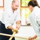 Two people practicing martial arts with wooden staffs indoors.
