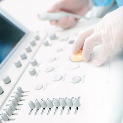 Person operates a medical ultrasound machine with gloved hands on the control panel.