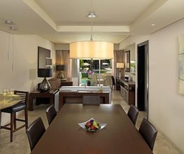 Comedor moderno con mesa, sillas, lámpara colgante y frutero. Cocina y sala al fondo.