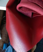 Tela roja enrollada en estante, junto a otras telas marrones y azules.