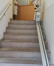 Mujer de pie en una recepción al final de una escalera con un elevador de silla al lado.