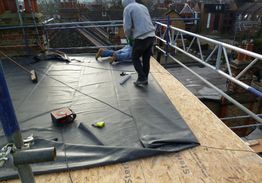 Workers installing a black rubber roof membrane on a building under construction.