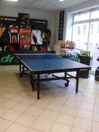 Tischtennisplatte in einem Sportgeschäft mit Sportkleidung an den Wänden.