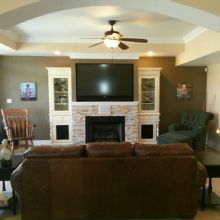 Living room with brown sofa, fireplace, TV, armchairs, and ceiling fan.