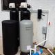 Outdoor water filtration system with two black and one gray tank connected to pipes.
