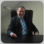 Ein Mann im Anzug sitzt an einem Schreibtisch und lächelt.