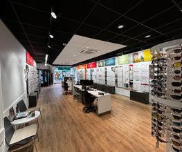 Optiekwinkel interieur met brillenrekken en tafels op houten vloer.