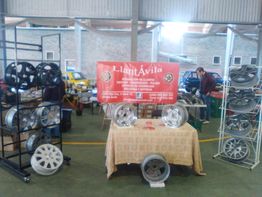Exhibición de llantas en un stand con banner rojo y mesas repletas de productos en un taller.
