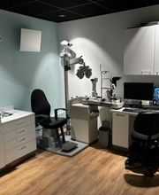 Optometriekamer met oogmeetapparatuur, bureau, stoelen, computer en opslagkasten.