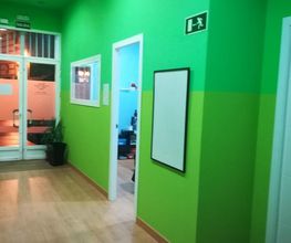 Pasillo interior con paredes verdes, una puerta y un cartel de salida de emergencia.