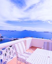 Vista al mar desde un balcón con sillas y mesa blanca bajo un cielo azul claro.