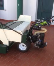 Macchina agricola verde e bianca su pavimento di mattonelle rosse, con maniglie e motore.