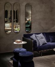 Elegantes Wohnzimmer mit blauem Sofa, Spiegeln und Hockern vor einer grauen Wand.