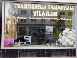 Schaufenster einer Thai-Massagepraxis mit goldener Buddha-Statue und weißem Blütenmotiv.