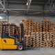 Yellow forklift in a warehouse next to stacks of wooden pallets.
