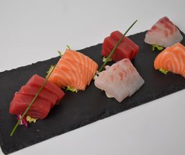 Surtido de sashimi de salmón, atún y pescado blanco sobre tabla negra.