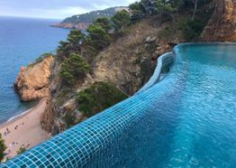 Piscina infinita con vista al mar y acantilados rocosos rodeados de árboles.