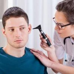 Doctor examining a man's ear with an otoscope in a clinical setting.