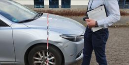 Mann mit Klemmbrett misst die Höhe eines silbernen Autos auf gepflastertem Parkplatz.