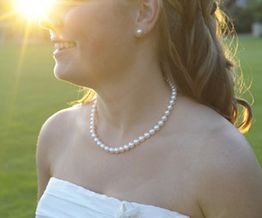 Eine Frau in einem weißen Kleid im Sonnenuntergang, trägt eine Perlenkette.