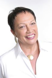 Eine lächelnde Person mit kurzen dunklen Haaren und weißem Hemd vor weißem Hintergrund.