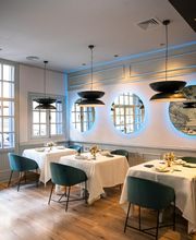 Restaurante elegante con mesas blancas, sillas verdes y espejos redondos iluminados en la pared.