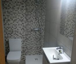 Baño moderno con ducha, lavabo y retrete. Pared con azulejos grises y marrones. Luz brillante.