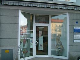 Geschäftseingang mit Glasfront, Werbeplakaten und Dienstleistungen wie Nagel- und Fußpflege.