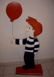 Holzfigur eines Jungen mit roten Haaren und gestreiftem Pullover, hält einen roten Luftballon.