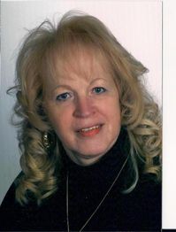 Eine Frau mit lockigem blondem Haar lächelt in die Kamera. Hintergrund ist neutral.