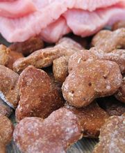 Herzförmige Hundekekse vor rohem Fleisch auf Holztisch.