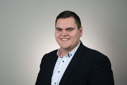 Ein lächelnder Mann in einem Anzug vor grauem Hintergrund.