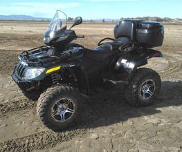 Cuatrimoto negra aparcada en terreno arenoso, fondo de paisaje con montañas distantes.
