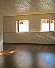 Leeres Zimmer mit Holzdecke und -boden, zwei offenen Fenstern, Lichtstrahlen, zentraler Säule.