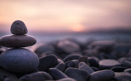 Stacked stones on a pebble beach with a soft, pink sunset in the background.