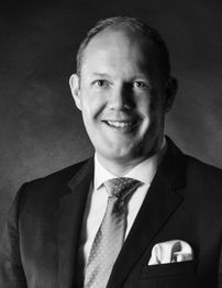 Porträt eines lächelnden Mannes im Anzug mit Krawatte und Einstecktuch, schwarz-weiß Foto.