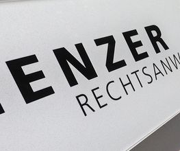 Schild mit der Aufschrift "Henzer Rechtsanwälte AG" an einer beigen Wand.