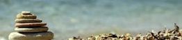 Steinbalance am Strand vor unscharfem blauem Wasser.