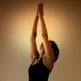Person bei Yogaübung mit erhobenen Armen vor orangefarbenem Hintergrund.