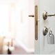 Open white door with a key in the lock and a blurred room in the background.