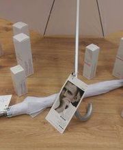 Weißer Regenschirm umgeben von weißen Produktverpackungen auf Holzboden.