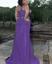 Mujer con vestido púrpura posando de espaldas en un entorno natural con árboles al fondo.