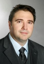 Mann in Anzug mit Krawatte vor grauem Hintergrund.