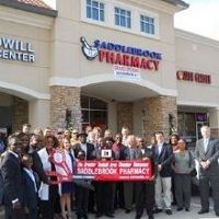 Group celebrating a ribbon-cutting at Saddlebrook Pharmacy outside a shopping center.