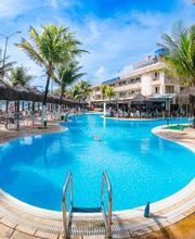 Piscina em resort tropical cercada por palmeiras, espreguiçadeiras e guarda-sóis.